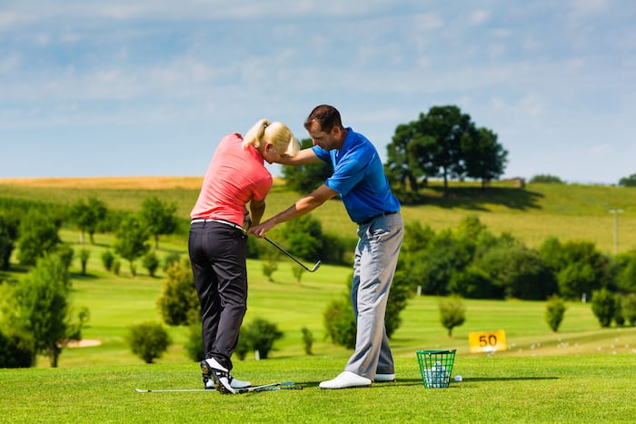 Young female golf player at Driving Range with a Golf Pro, she presumably does exercise